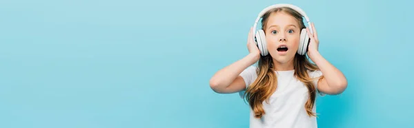 Geschokt Meisje Wit Shirt Aanraken Draadloze Hoofdtelefoon Geïsoleerd Blauw Panoramisch — Stockfoto