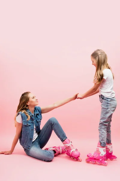 Hija Cogida Mano Madre Caída Sentada Suelo Patines Sobre Rosa — Foto de Stock