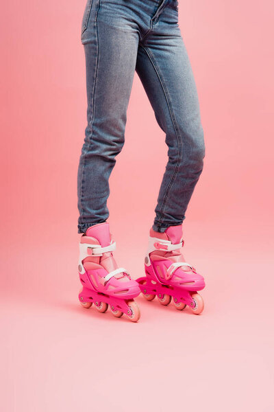 cropped view of woman in jeans and rollers skates on pink