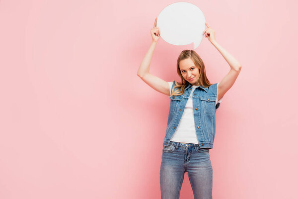 young woman in denim clothes holding thought bubble above head isolated on pink