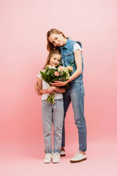 全景年轻女子身穿牛仔服装 送花给女儿 拥抱她的粉色 — 图库照片