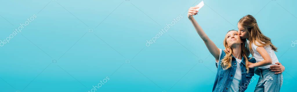 Horizontal image of child kissing mother taking selfie on smartphone isolated on blue — Stock Image Horizontal Image Child Kissing Mother Taking Selfie Smartphone Isolated Blue Stock Image