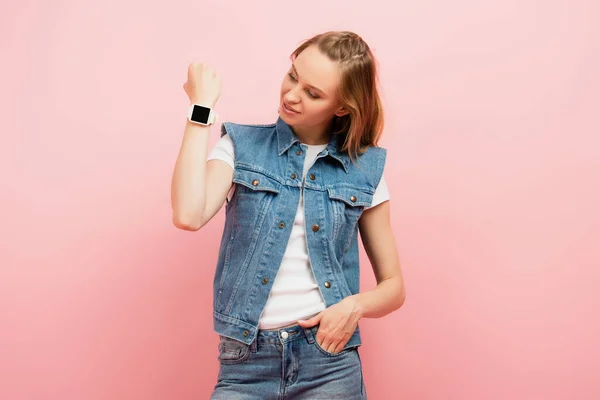 Młoda Kobieta Dżinsowej Kamizelce Pokazuje Smartwatch Nadgarstku Stojąc Ręką Kieszeni — Zdjęcie stockowe