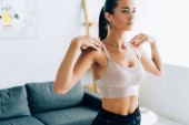 Žena ve sportovním oblečení zahřívá před cvičením doma 