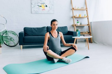 Evde yoga yapan hamile bir kadın spor minderinde poz veriyor. 