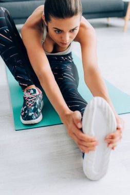 Genç sporcunun seçici odak noktası oturma odasındaki spor minderinin üzerinde bacağını esnetmesi. 