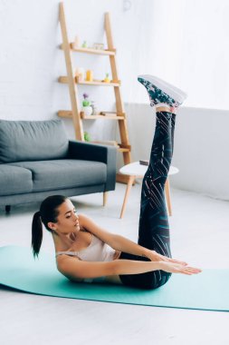 Kalkmış bacaklı genç bir kadın oturma odasında karın kası yapıyor. 