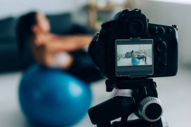 Dijital kameranın seçici odak noktası spor kadının yanında oturma odasında fitness topuyla çalışıyor. 