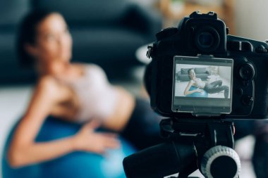 Spor salonunun yanındaki tripodun üzerinde dijital kameranın seçici odak noktası evde fitness topu eğitimi. 