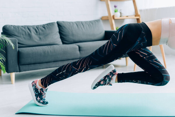 Обрезанный вид пригодной женщины в спортивной одежде и кроссовки тренировки на фитнес-мат в гостиной 