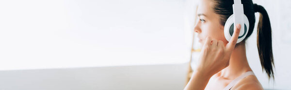 Horizontal crop of young woman touching headphones at home 