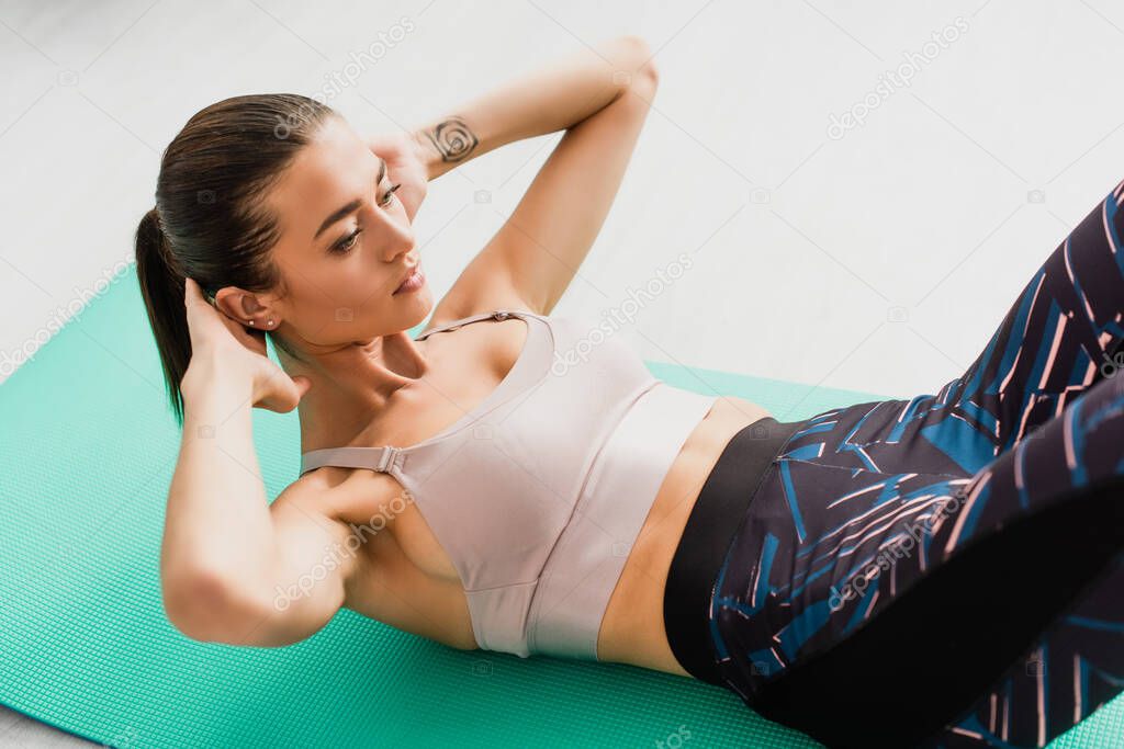 Selective focus of brunette sportswoman doing abs on fitness mat on floor