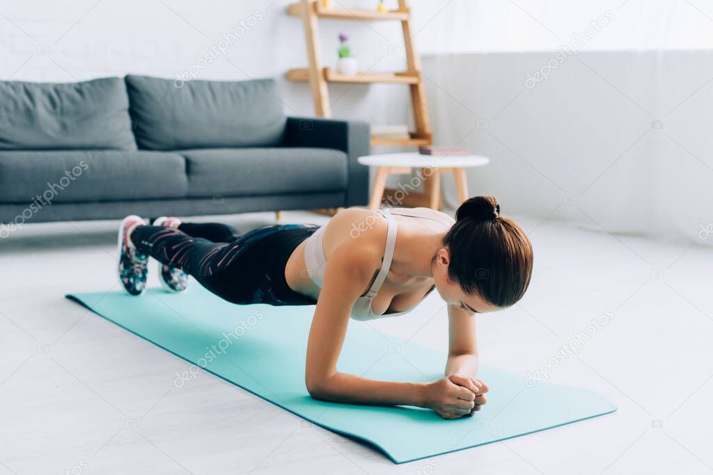 Selective focus of sportswoman doing plank on fitness mat at home 