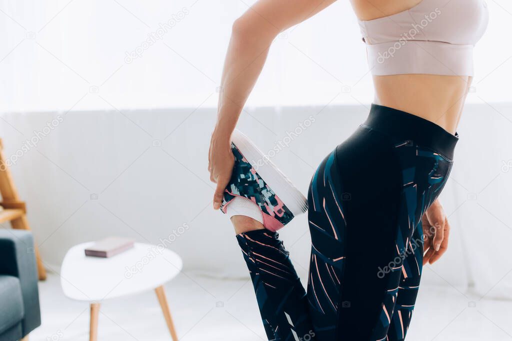 Cropped view of fit sportswoman stretching leg in living room 