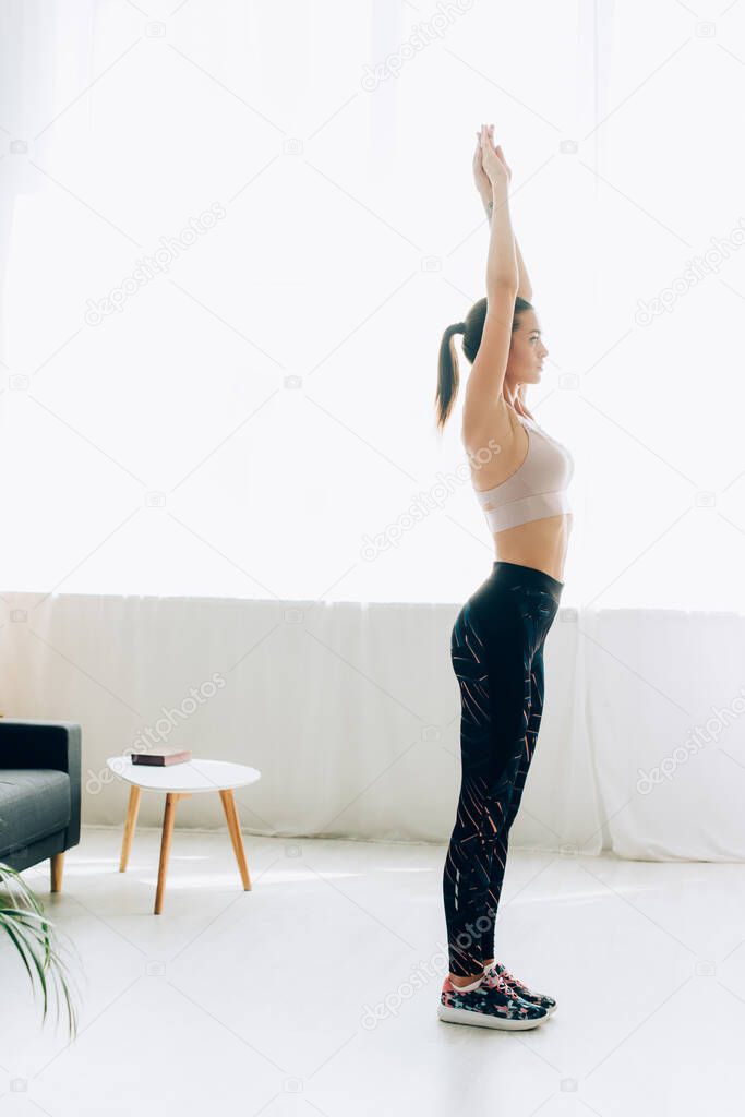 Side view of sportswoman standing with raised hands in living room 