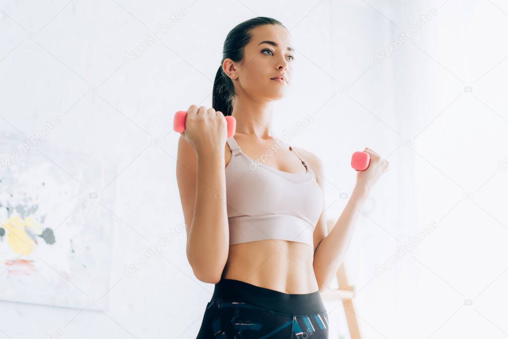 Concentrated sportswoman exercising with dumbbells at home 