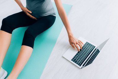 Hamile bir kadının evdeki spor paspası olarak dizüstü bilgisayar kullanması görüntüsü. 