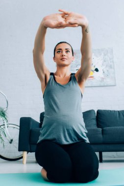 Genç hamile kadının seçici odak noktası evde fitness minderinde oturuyor. 