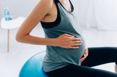 Evde spor salonunda antrenman yaparken karnına dokunan hamile bir sporcunun görüntüsü. 