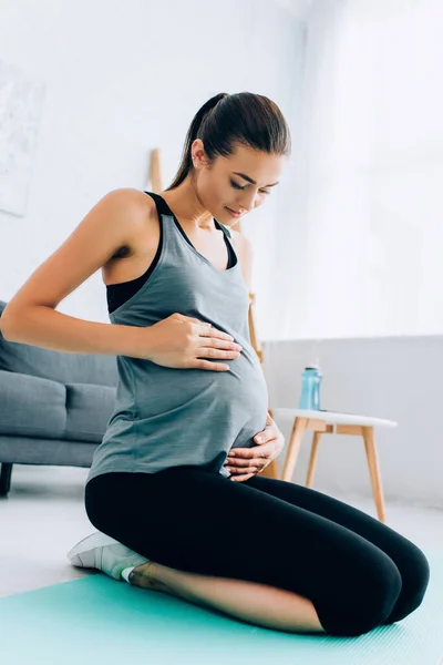 Hamile Sporcu Kadın Oturma Odasındaki Spor Minderinde Otururken Karnına Dokunuyor — Stok fotoğraf