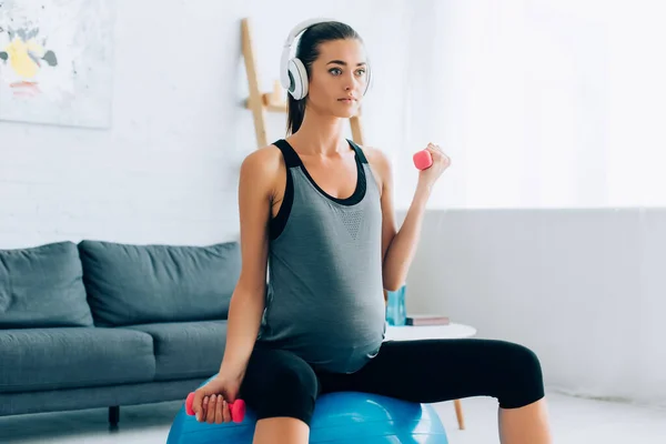 Schwangere Sportlerin Beim Kopfhörertraining Mit Hanteln Und Fitnessball Hause — Stockfoto