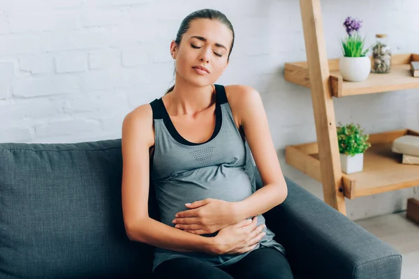 Tired Sportswoman Embracing Belly While Sitting Couch Home — Stock Photo, Image