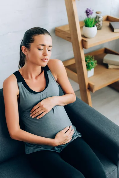 怀孕的女运动员感到痛楚 抱着肚子躺在沙发上 — 图库照片