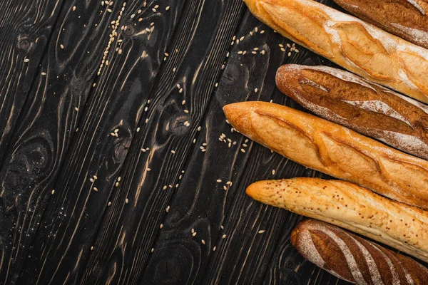 top view of fresh baked baguette loaves on wooden black surface