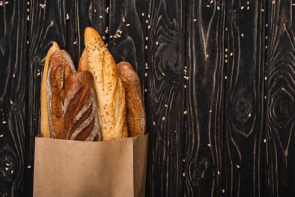 top view of fresh baked baguette loaves in paper bag on wooden black surface