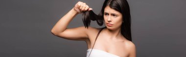 upset brunette long haired woman looking at split ends isolated on black, panoramic shot clipart
