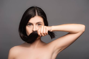 naked brunette woman holding hair near face isolated on black clipart