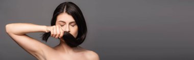 naked brunette woman with closed eyes holding hair near face isolated on black, panoramic shot clipart