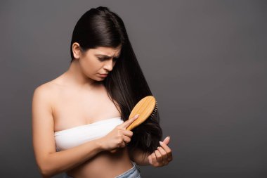 worried brunette woman brushing hair isolated on black clipart