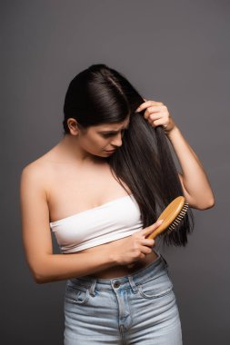 worried brunette woman brushing hair isolated on black clipart