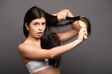 shocked brunette woman brushing hair isolated on black clipart