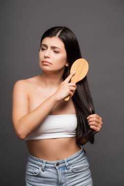 sad brunette woman brushing hair isolated on black clipart