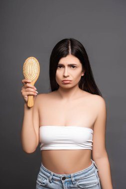 sad brunette woman holding hairbrush isolated on black clipart