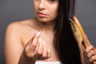 selective focus of brunette woman holding lost hair while brushing isolated on black clipart