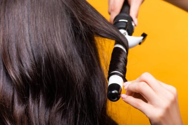 cropped view of hairdresser using curling iron isolated on yellow clipart
