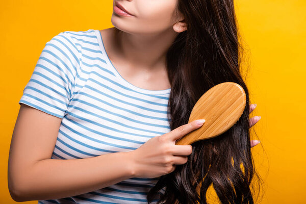 cropped view of brunette woman brushing hair isolated on yellow