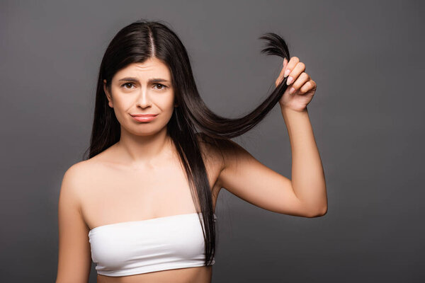 upset brunette long haired woman showing split ends isolated on black