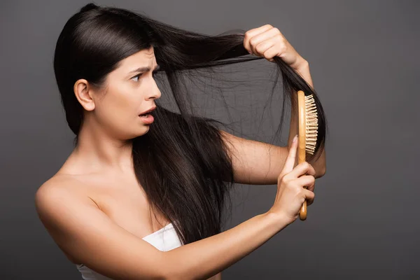 shocked brunette woman brushing hair isolated on black
