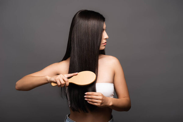 cropped view of brunette woman brushing shiny hair isolated on black