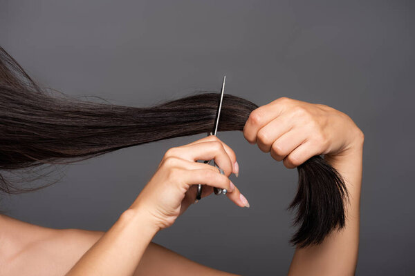 cropped view of naked brunette woman cutting hair isolated on black
