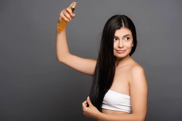 Mulher Morena Pulverizando Óleo Cabelo Isolado Preto — Fotografia de Stock