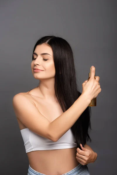 brunette woman spraying oil on hair isolated on black