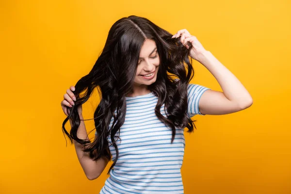 Morena Mujer Endureciendo Pelo Largo Rizado Sonriendo Aislado Amarillo — Foto de Stock