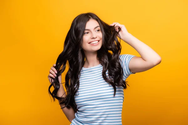 Morena Mujer Endureciendo Pelo Largo Rizado Sonriendo Aislado Amarillo — Foto de Stock