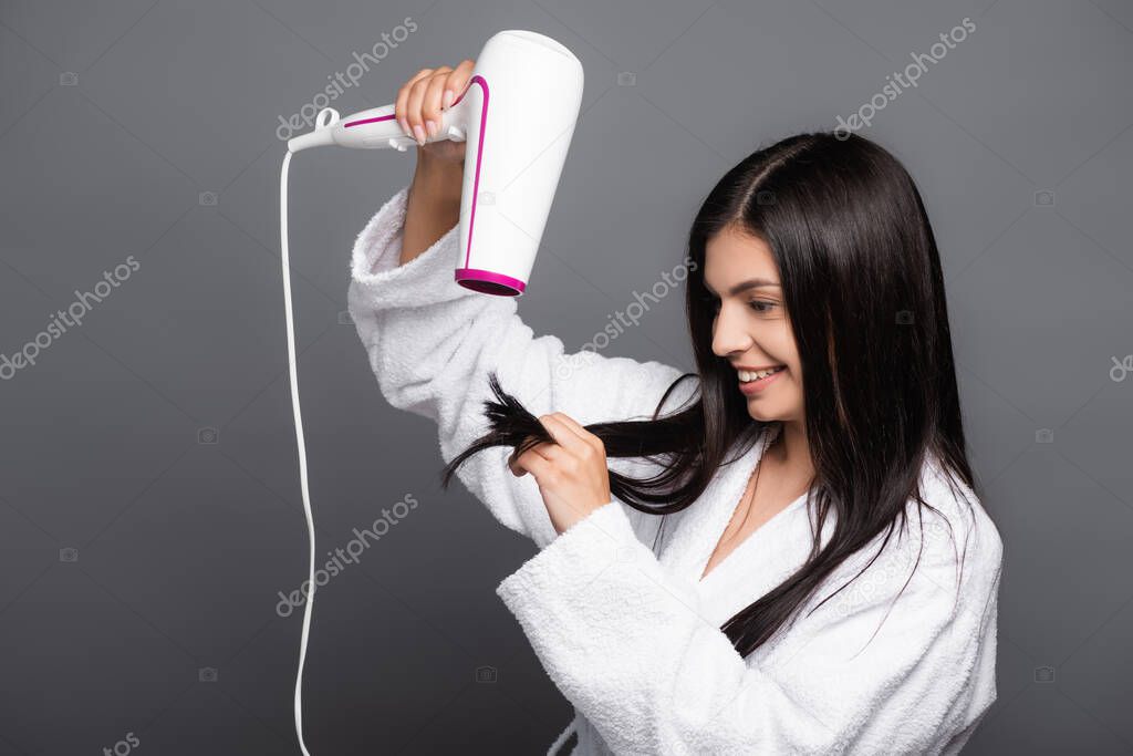 brunette long haired woman in bathrobe using hairdryer isolated on black