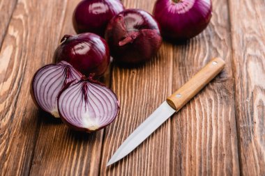 cut and whole red onion near knife on wooden table clipart